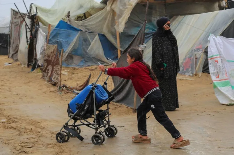 A girl uses a baby stroller to ferry drinking water in rainy weather at a makeshift tent camp in Rafah in the southern Gaza Strip on Friday. AFP
