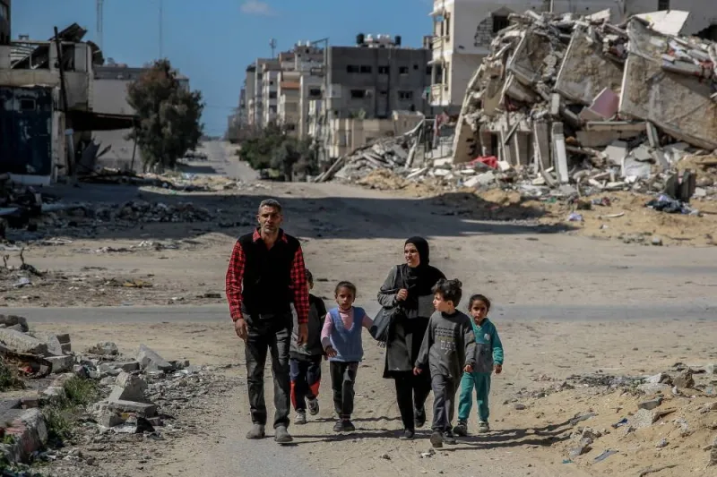 A Palestinian family walk past buildings destroyed in previous Israeli strikes as they collect things rescued from the rubble and wood in Gaza City, Monday. AFP