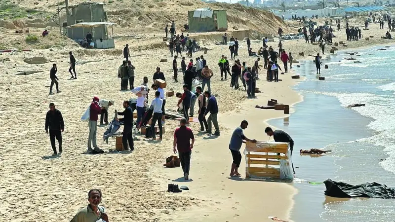 Palestinians gather on a beach as they collect aid airdropped by an airplane,  in the northern Gaza Strip