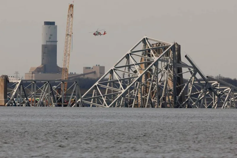 A Coast Guard helicopter flies past a floating crane as it works on the twisted remains of the Francis Scott Key Bridge, which was destroyed when a cargo ship collided with it earlier this week, on Friday. AFP