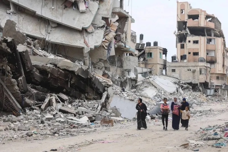Palestinian women and children walk past the ruins of buildings in Gaza City Monday.