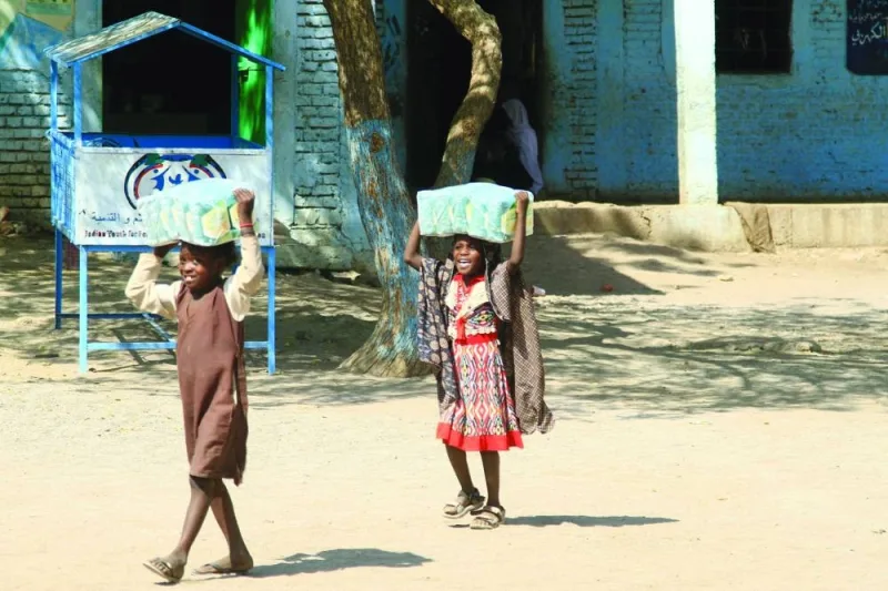 Children carry packs of humanitarian aid at the school housing displaced Sudanese who fled violence in war-torn Sudan, near the eastern city of Gedaref, in a file picture.