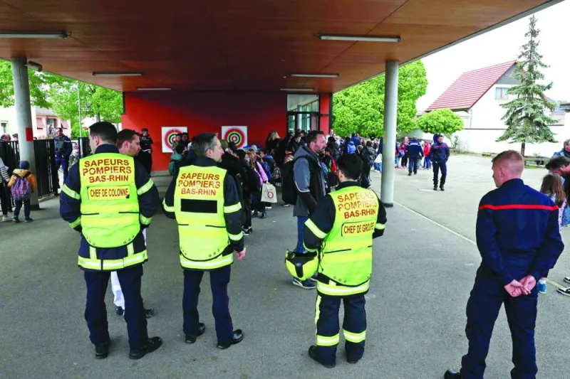 
Parents collect their children with police officers and a firefighter keeping watch at a school in the eastern France city of Souffelweyersheim, after two girls were wounded in a knife 
attack outside the school. 