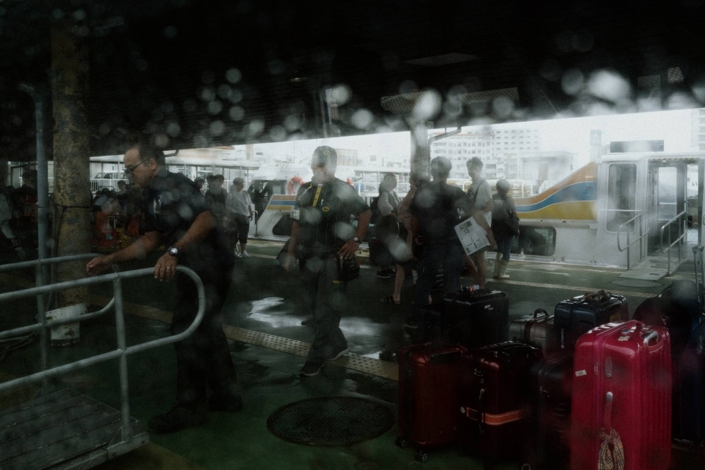 Staff unload luggage from a ferry at Ishigaki terminal on a rainy day.