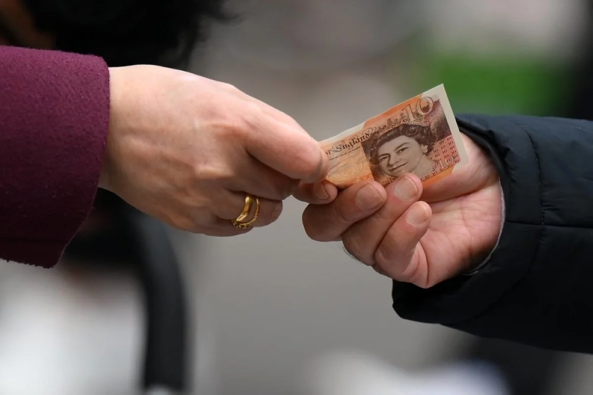 LONDON: A customer uses a ten pound note to pay for goods at a market in east London. -- AFP