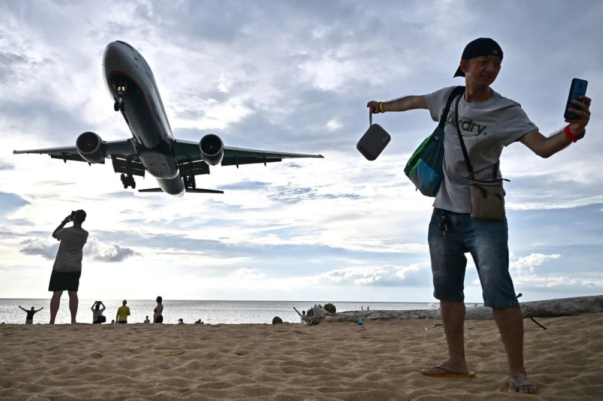 PHUKET: This photograph taken on November 18, 2023, shows a tourist taking a selfie on the Mai Khao Beach as an airplane lands at Phuket International Airport in the southern Thai island of Phuket. -- AFP