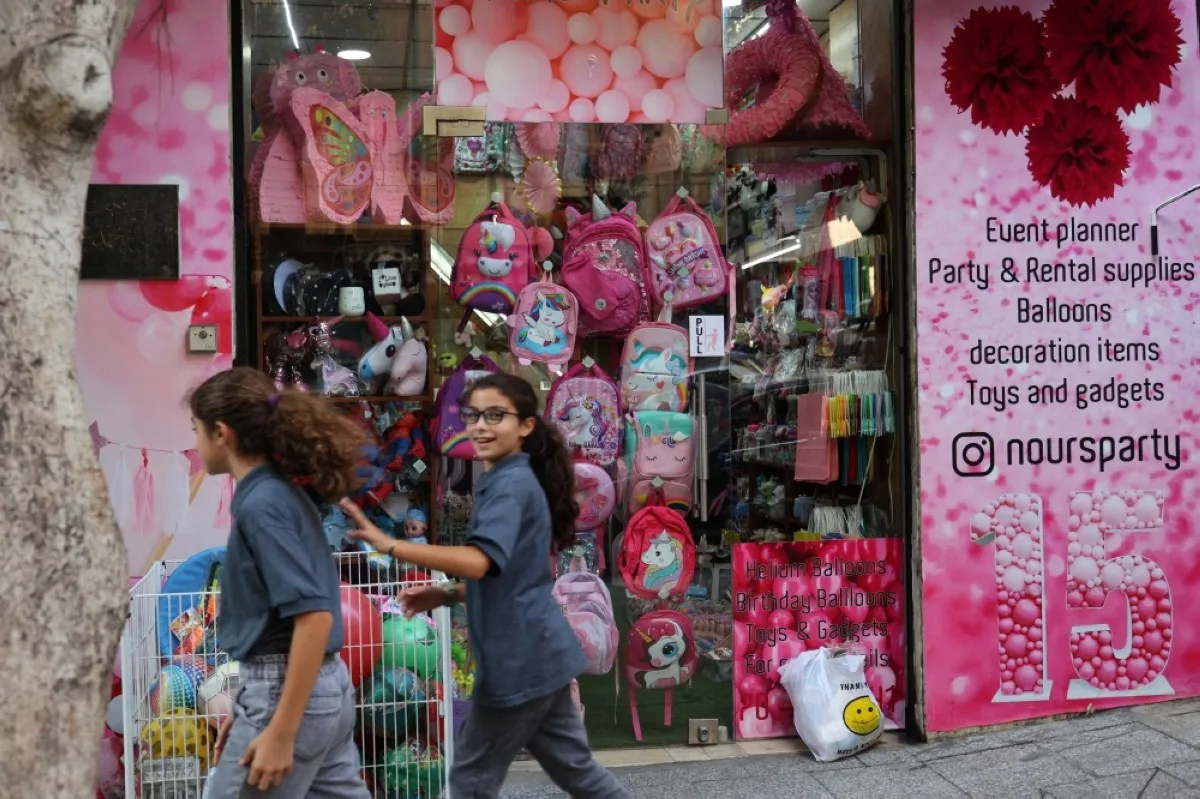 BEIRUT: Two girls walk past a stationary shop in Beirut.- AFP