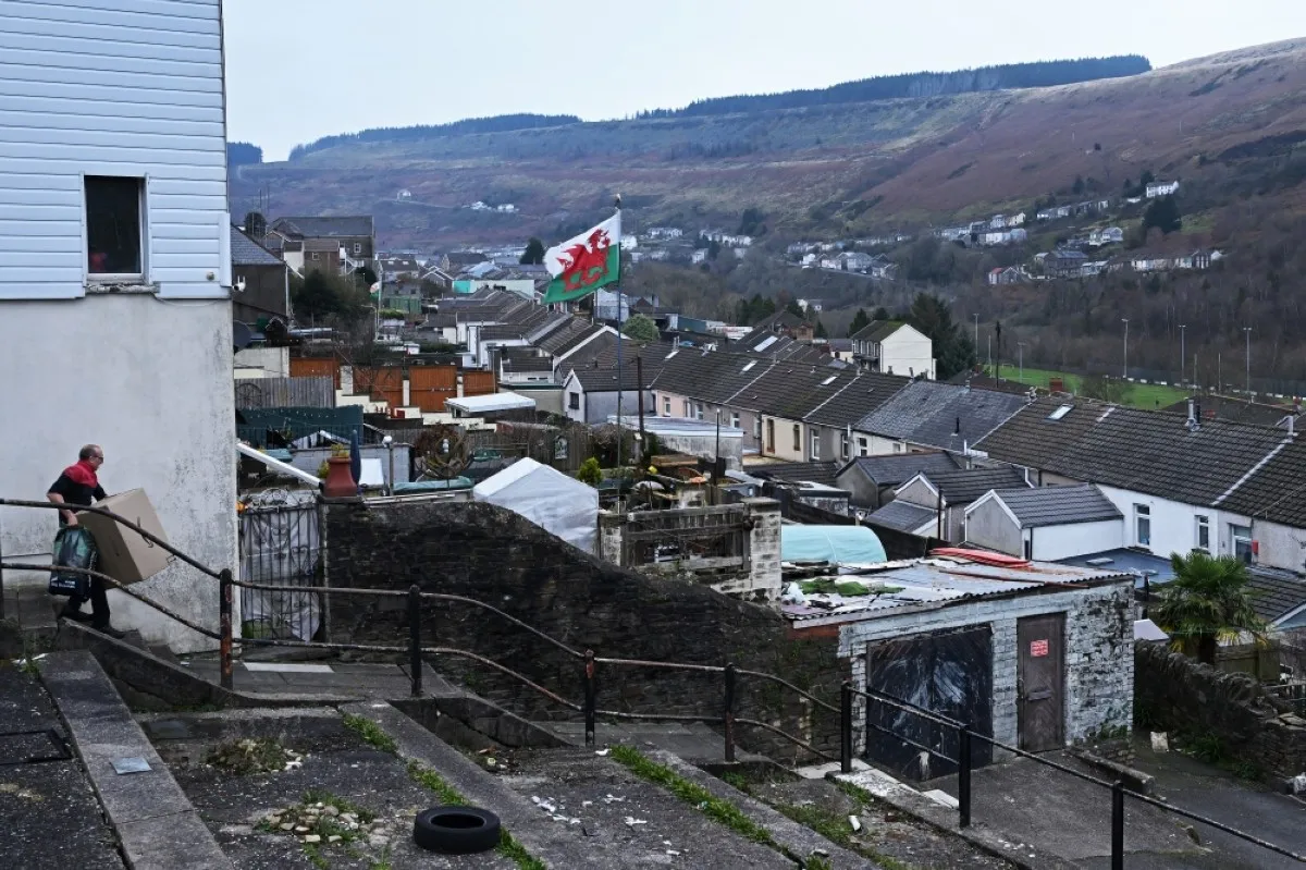 RHONDDA, UK: A delivery driver carries a box down a flight of steps in Tylorstown near the Tylorstown tip on December 6, 2023 in the Rhondda Valley, south Wales. – AFP