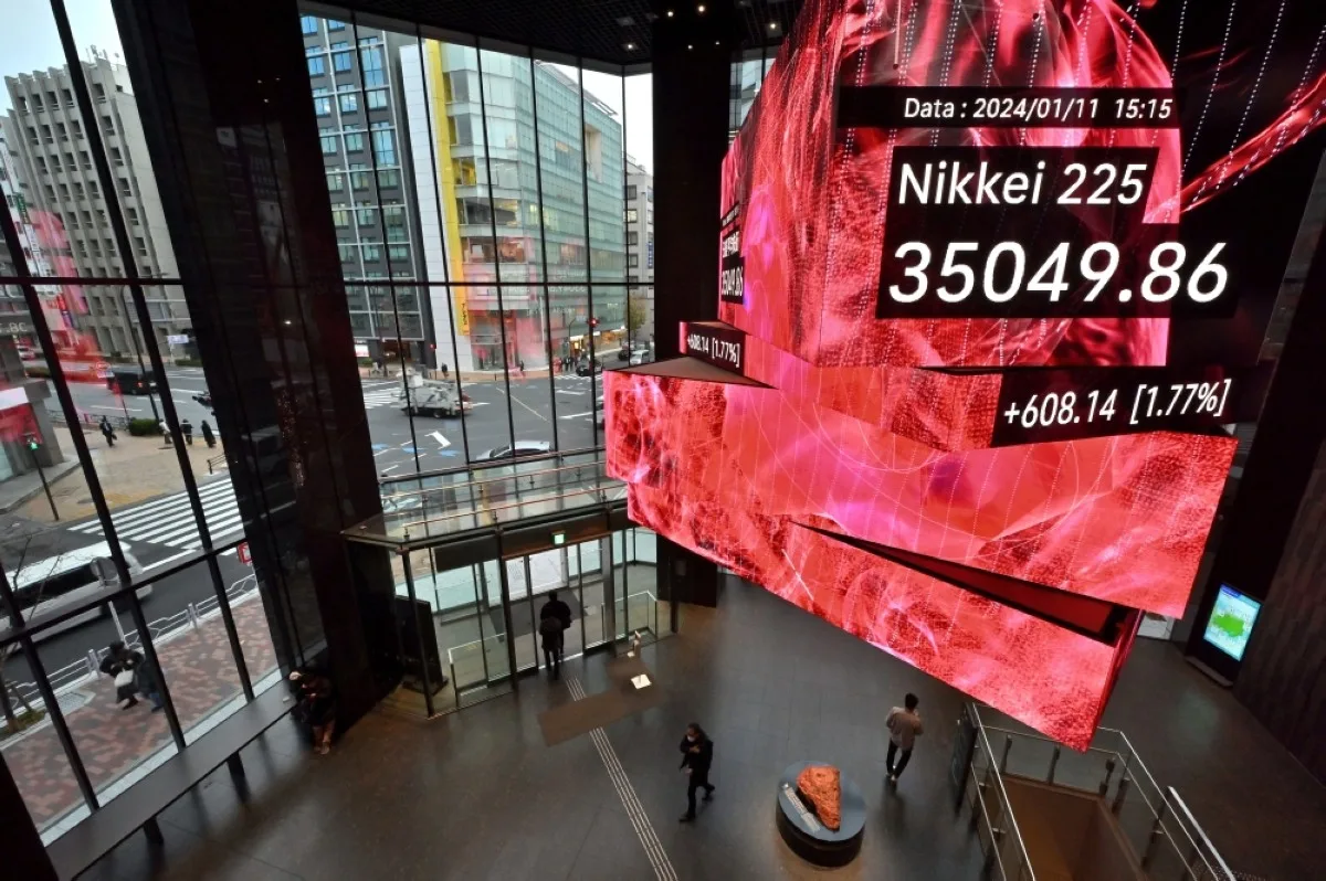 TOKYO: Pedestrians walk below a signboard showing the closing numbers on the Tokyo Stock Exchange, along a street in Tokyo in January 11, 2024. -- AFP