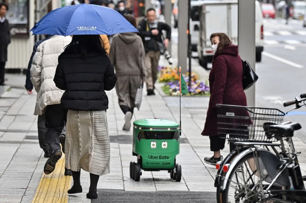 Pedestrians walk alongside an unmanned robot (C) as it navigates down a street during a demonstration of a robot delivery service by Uber Eats Japan, Mitsubishi Electric and robot developer Cartken in downtown Tokyo on March 5, 2024. -- AFP