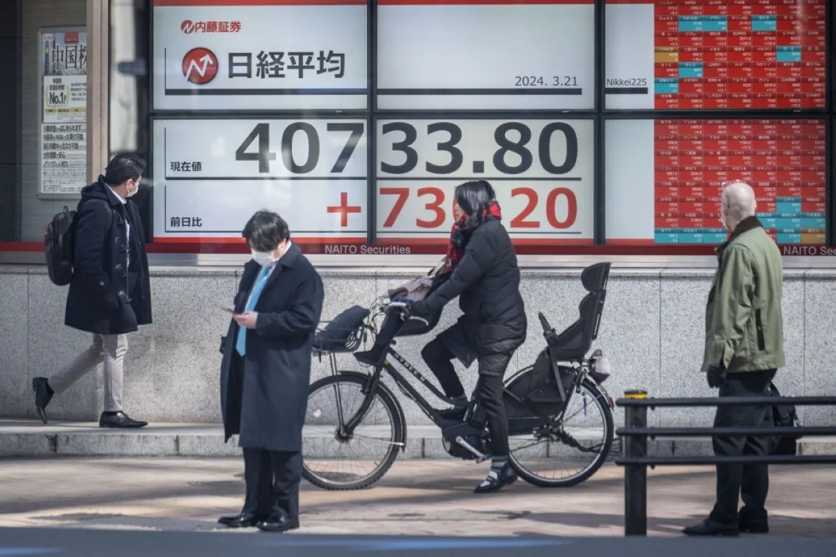 TOKYO: People walk past an electronic board showing a share price of the Nikkei index of the Tokyo Stock Exchange in Tokyo. – AFP