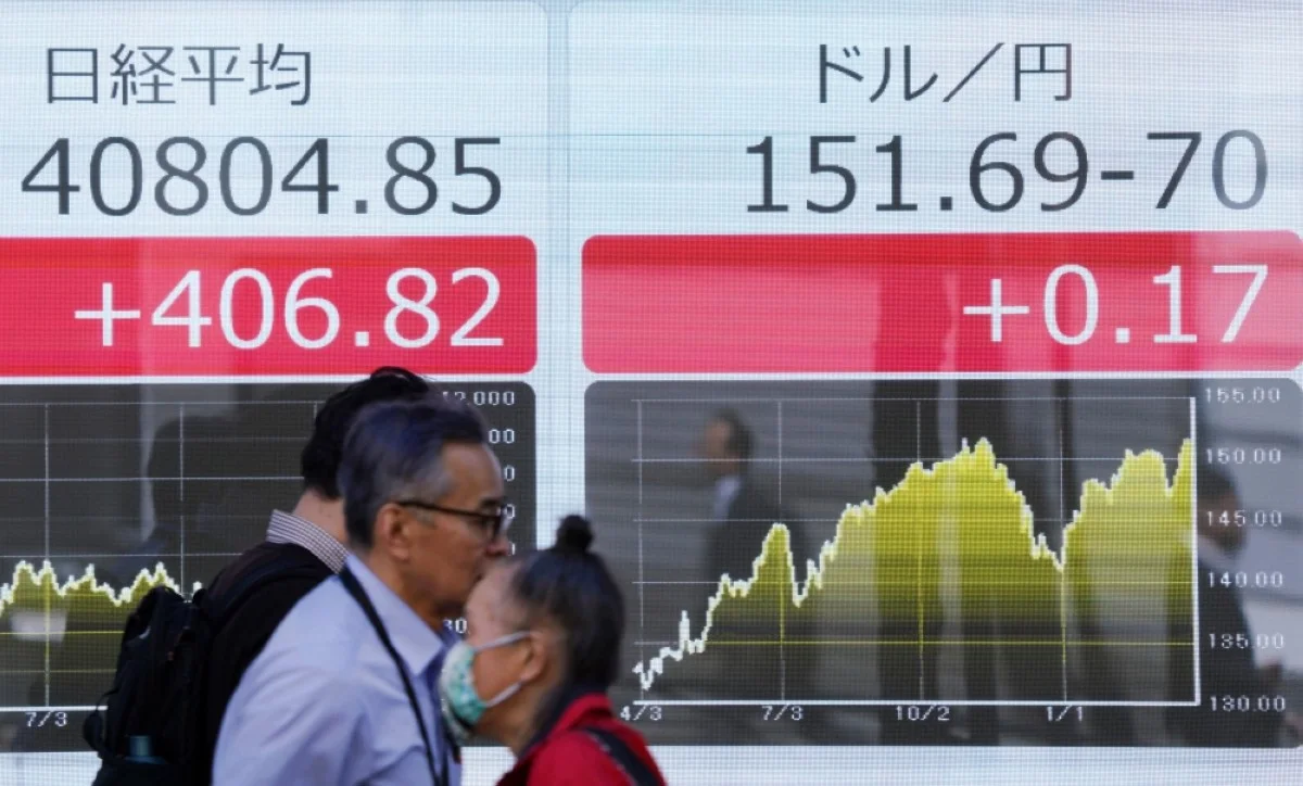 TOKYO: People walk past an electronic board showing a share price of the Nikkei index of the Tokyo Stock Exchange (left) and the rate of the Japanese yen versus the US dollar (right) along a street in Tokyo on March 27, 2024. –AFP