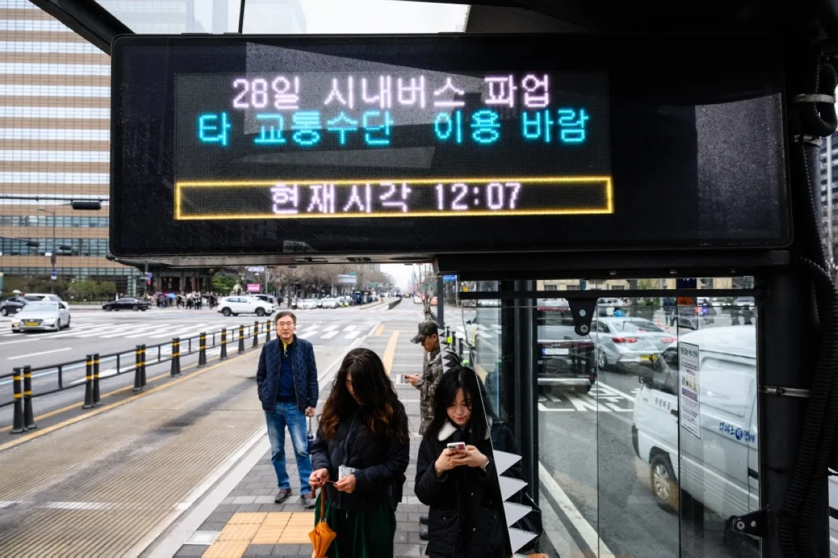 SEOUL: Commuters stand at a bus stop with an electronic display that reads "28th city bus on strike. -- AFP