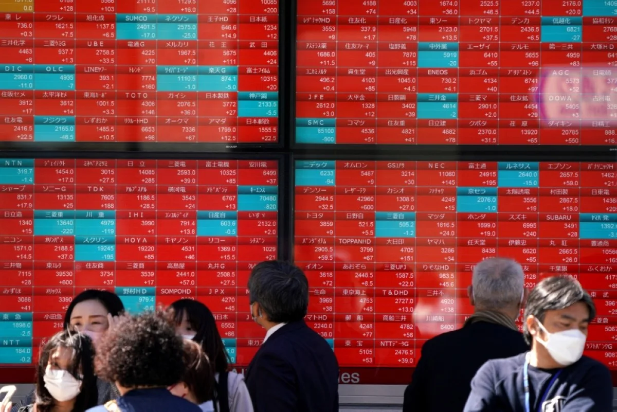 TOKYO: People stand in front of an electronic board displaying stock prices of Nikkei 225 listed on the Tokyo Stock Exchange along a street in Tokyo. – AFP