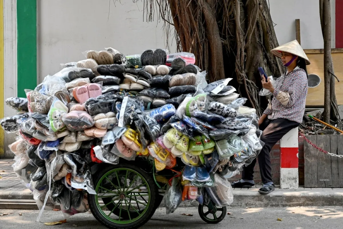 HANOI: A shoe street vendor uses her phone as she waits for customers along a street in Hanoi.- AFP