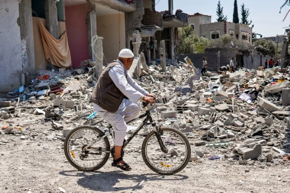 GAZA: A man rides a bicycle past the rubble of a collapsed building in the eastern side of the Maghazi camp for Palestinian refugees in the central Gaza Strip on April 15, 2024.- AFP