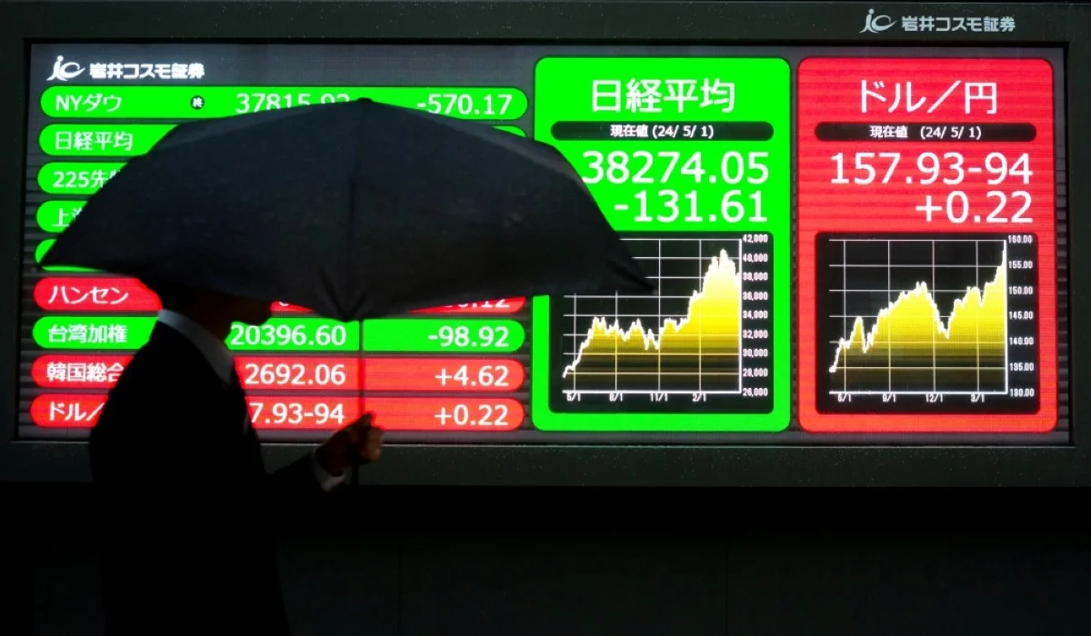 TOKYO: A man walks in front of electronic boards?displaying the exchange rate for the Japanese yen against the US dollar (R) and the closing numbers of Tokyo Stock Exchange share price (second right) in Tokyo. – AFP