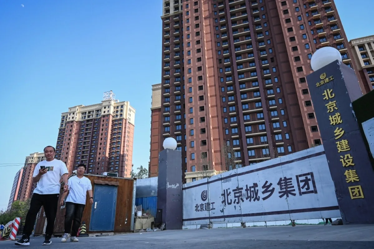 People walk past a housing complex under construction in Beijing on May 17, 2024. -- AFP