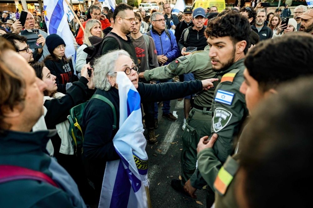 As Israel breaches ceasefire and intensifies Gaza attacks with no restraint from US, what options are left for Hamas? A woman carrying a flag speaks to Israeli security forces as they try to disperse a demonstration against Prime Minister Benjamin Netanyahu and calling for an end to the war in Gaza on March 19, 2025. — AFP pic