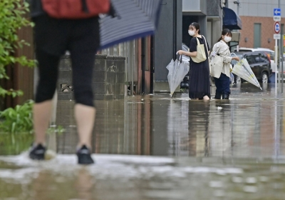 Pedestrians walk on a flooded road in the city of Akita on Sunday morning after heavy rains hit the area. 