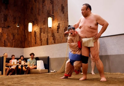 Nadine, a 43-year-old tourist from the U.S., wears a sumo wrestler costume and tries to spar against former sumo wrestler Towanoyama in the sumo ring at Yokozuna Tonkatsu Dosukoi Tanaka in Tokyo in June 30.