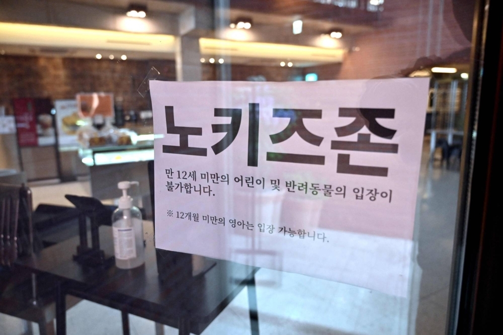 A "No Kids Zone" sign written in Korean hangs on the glass door of a cafe in Gimpo, South Korea.
