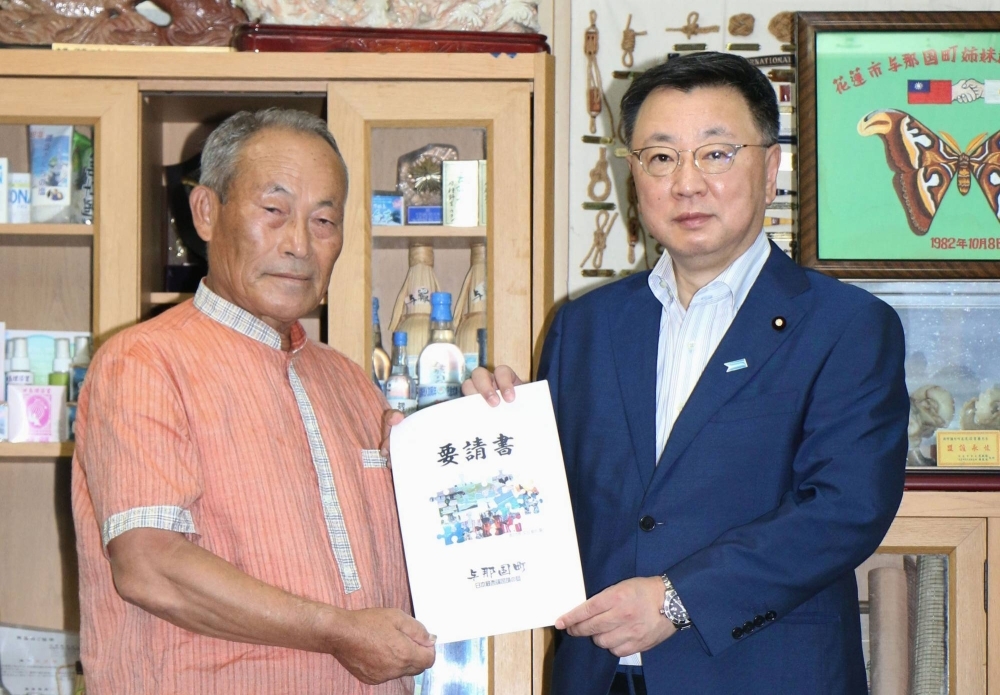 Mayor Kenichi Itokazu (left) hands a petition for building shelters to Chief Cabinet Secretary Hirokazu Matsuno, in Yonaguni on Sunday.