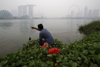 A man catches a fish along the bank overlooking the Singapore skyline shrouded by haze in 2015. 