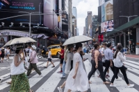 Pedestrians hold umbrellas for protection from the sun during a heat wave in New York on Thursday. | Bloomberg
