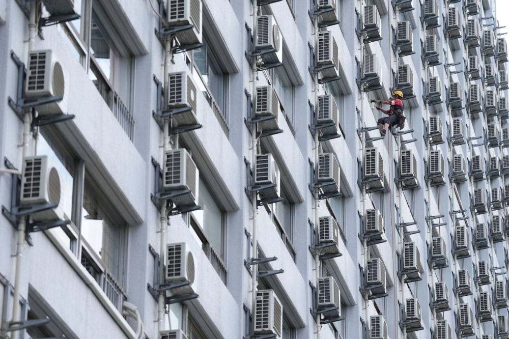A worker washes windows next to air conditioning units at an apartment building in Tokyo on July 21.