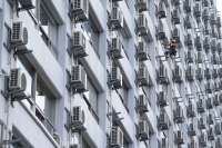 A worker washes windows next to air conditioning units at an apartment building in Tokyo on July 21. | Bloomberg