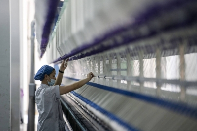 A worker stands in front of a machine on a yarn production line in Putian, Fujian province, China, in February 2021.