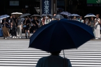 People use umbrellas and parasols to seek relief from soaring temperatures while waiting to cross a street outside Tokyo's Shinjuku Station last week. | AFP-JIJI