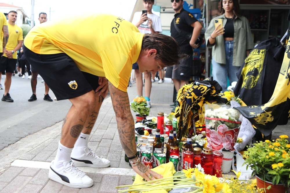 An AEK Athens player places flowers outside Agia Sophia Stadium in memory of a fan who died in a Monday-night brawl in Athens on Tuesday.