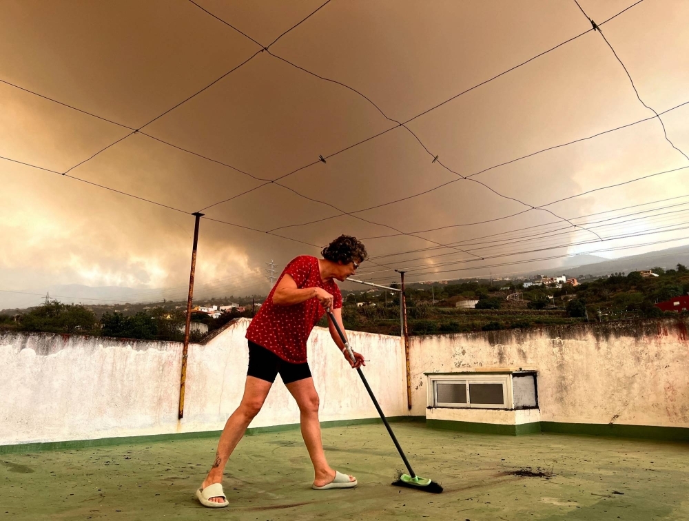 A woman sweeps ash off the terrace of her house while smoke rises over the village of Benijos as wildfires rage out of control on Spain's Tenerife on Saturday. 