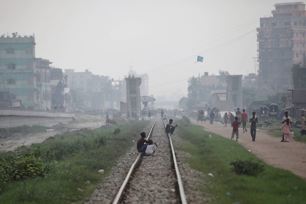 People sit on a rail track as smoke rises from steel mills near a slum in Dhaka, Bangladesh, on Tuesday.