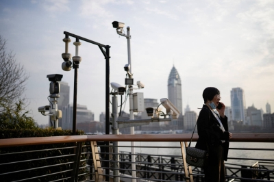 A woman stands under surveillance cameras on a riverside, during the National People's Congress in Shanghai on March 7.