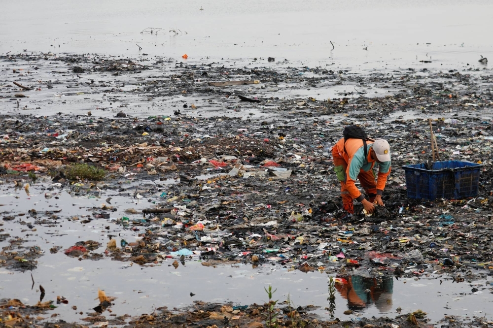 A municipality worker collects garbage, most of which is plastic and domestic waste, along the shore of Jakarta.