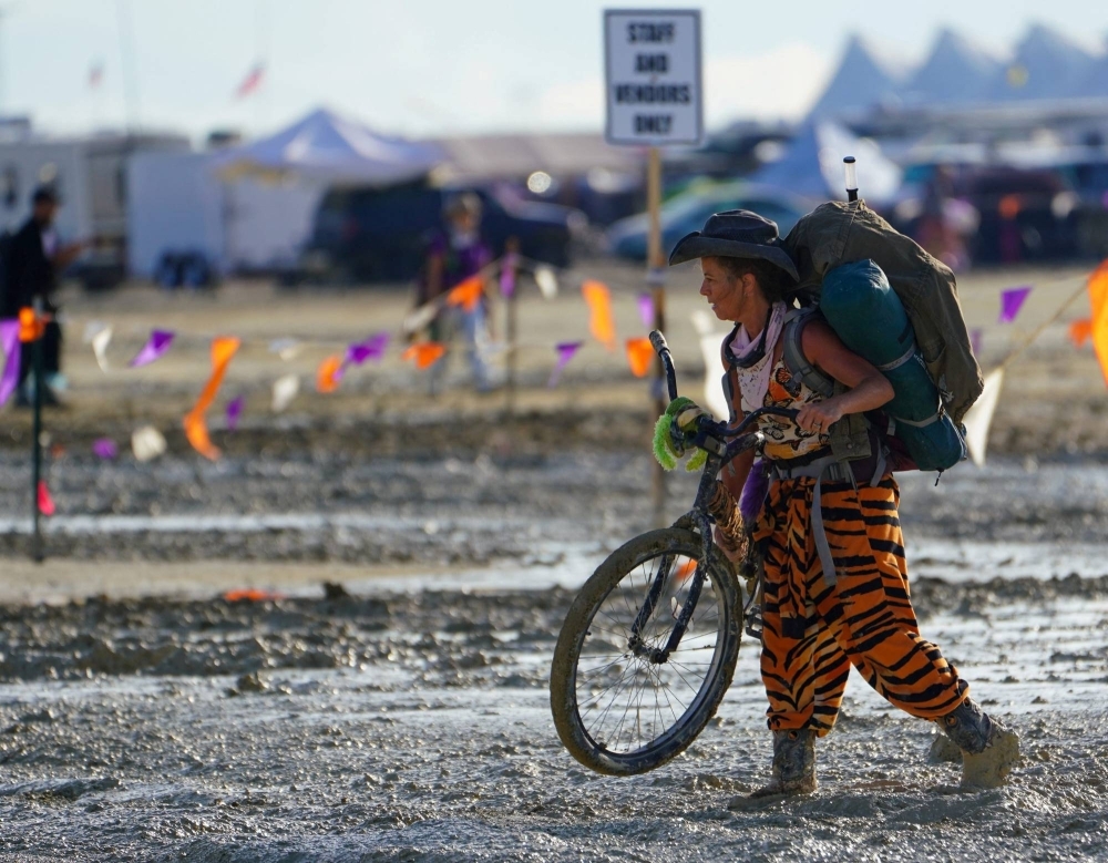 A Burning Man participant walks their bike through mud near the exit, after a severe rainstorm left tens of thousands of revelers attending the annual festival stranded in mud in Black Rock City in the Nevada desert.
