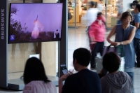 Passengers wait for their train in front of a TV broadcasting a news report on North Korea firing a ballistic missile, at the main railway station in Seoul in July. | REUTERS