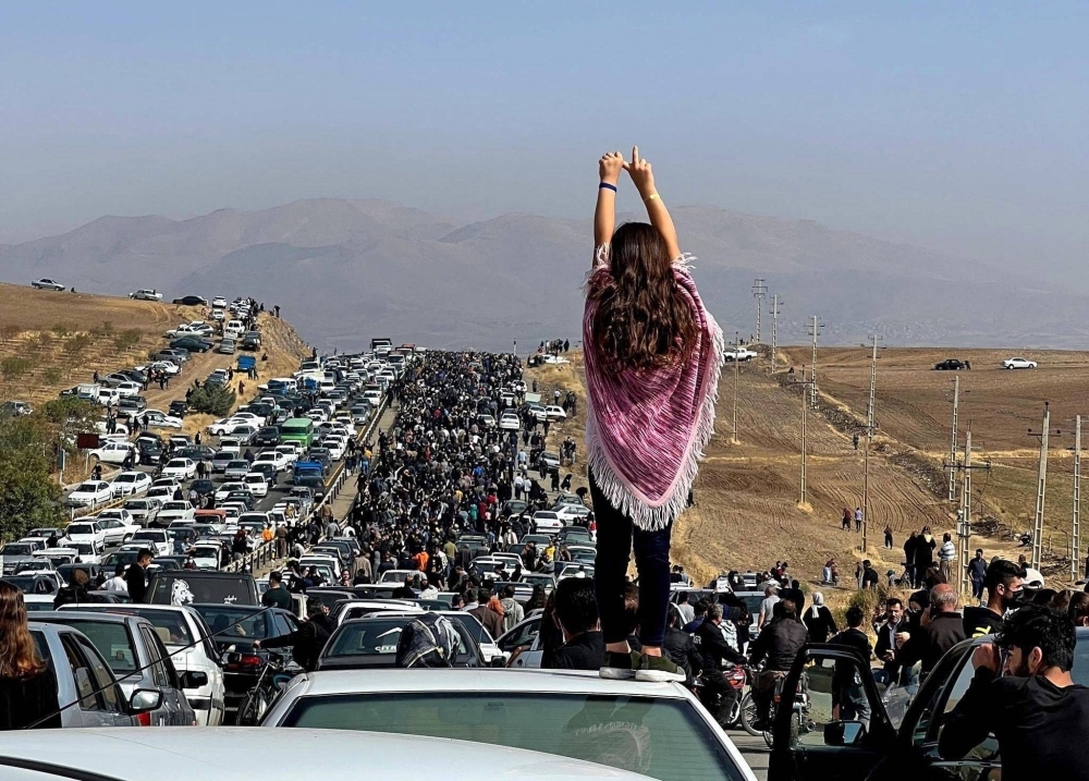 An unveiled woman stands on top of a vehicle on Oct. 26, 2022, as thousands make their way toward Aichi cemetery in Saqez, Mahsa Amini's hometown in the western Iranian province of Kurdistan, to mark 40 days since her death.