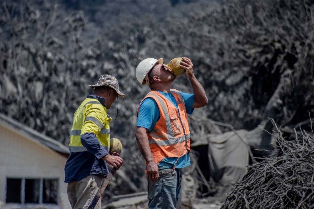 A worker drinks coconut water during relief work following a volcanic eruption and tsunami in Nomuka, Tonga, in January 2022.