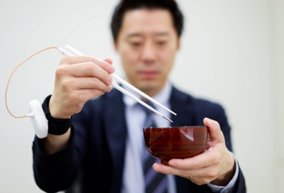 An employee of Kirin Holdings demonstrates chopsticks that can enhance food taste using an electrical stimulation waveform that was jointly developed by the company and Meiji University's School of Science and Technology Prof. Homei Miyashita, in Tokyo in April 2022.