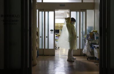 A nurse puts on protective clothing in front of an isolated hospital room to examine a person who tested positive for COVID-19 at a hospital in Saitama Prefecture in July 2021.