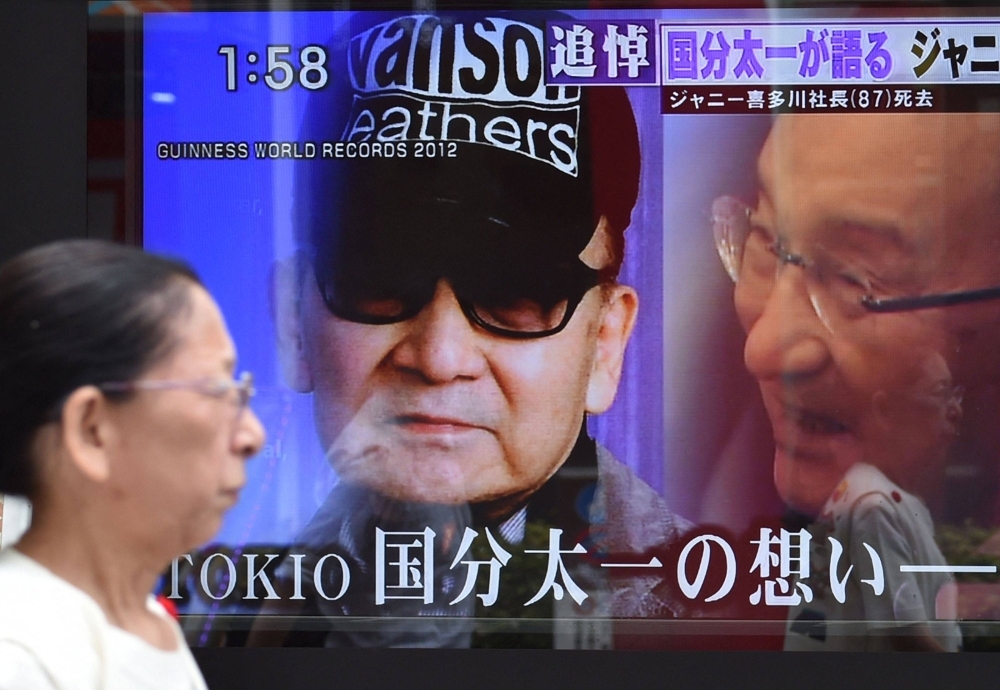 A woman walks past a roadside television screen reporting the death of Johnny Kitagawa, founder of Japanese talent agency Johnny & Associates, in Tokyo in July 2019. 