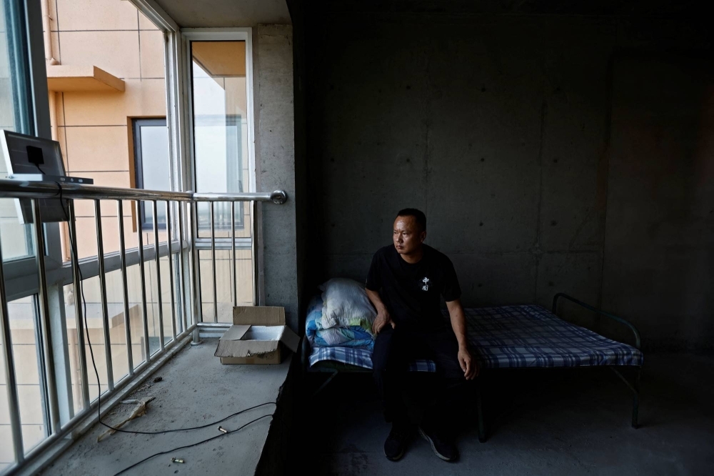 Shi Tieniu, 39, sits in a room of an unfinished residential building at Gaotie Wellness City complex in Tongchuan, Shaanxi province, China.
