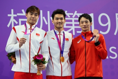Bronze medalist Ryosuke Irie (right) celebrates on the podium with bronze medalist Wang Gukailai (left) and gold medalist Xu Jiayu, both of China, after the men's 50-meter backstroke final at the Asian Games in Hangzhou, China, on Monday.