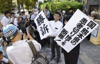 Lawyers representing plaintiffs of a lawsuit demanding damages after being rejected from a special Minamata disease relief program as sufferers of the disease hold up signs in front of the Osaka District Court on Wednesday. | Kyodo