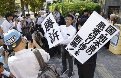 Lawyers representing plaintiffs of a lawsuit demanding damages after being rejected from a special Minamata disease relief program as sufferers of the disease hold up signs in front of the Osaka District Court on Wednesday.