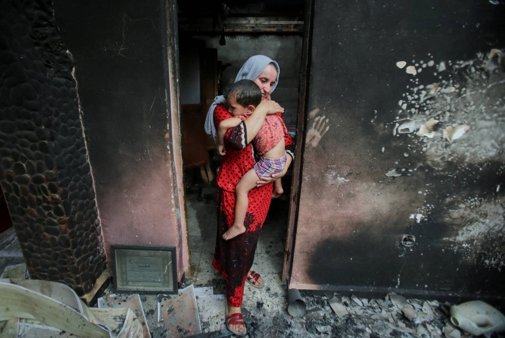 A mother carries her child inside her burnt house, following a wildfire in Bejaia, Algeria, on July 25